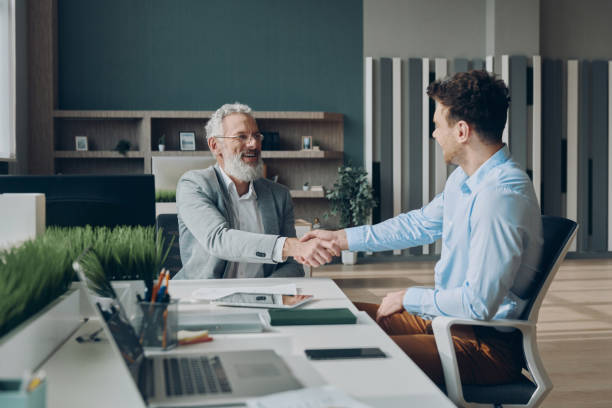 istock Two happy businessmen shaking hands while sitting at the office desk together 1471405723