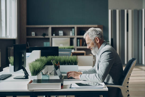 istock Confident mature businessman working on laptop while sitting at his working place in office 1471405794