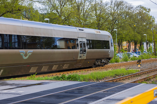 Uppsala. Sweden. Europe. 05.14.2022. Close up view of outgoing speed electric train passing crossroad in town.