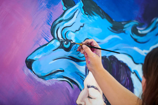 Woman artist hand holds paint brush and draws surreal fantasy image on canvas stock photo