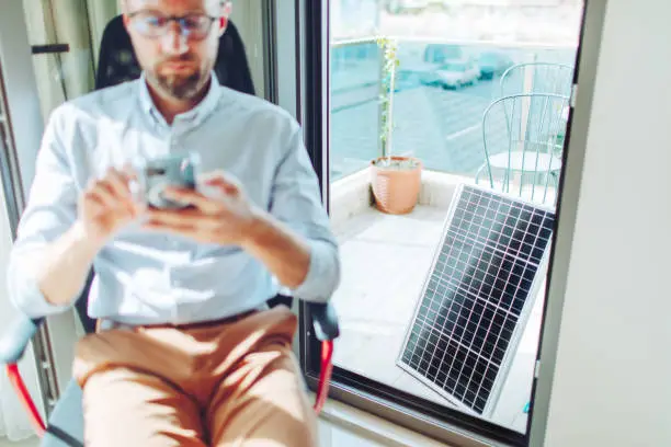 Sustainable lifestyle, young adult man using mobile with solar panel at background