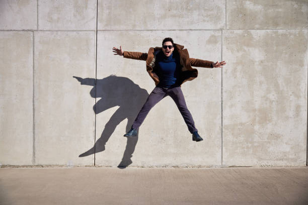 istock Excited man jumping against concrete wall wearing coat during sunny afternoon 1471409048