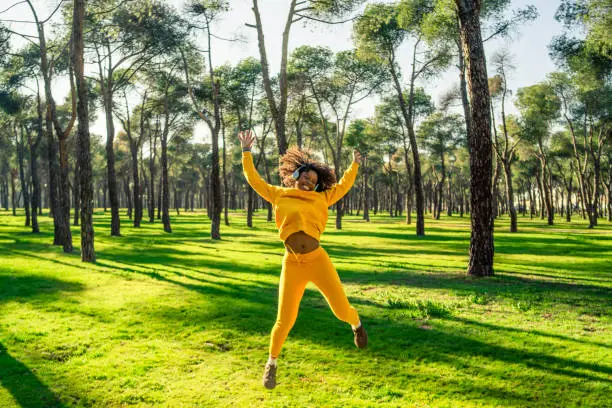 A girl in a yellow tracksuit jumping for joy in the park.