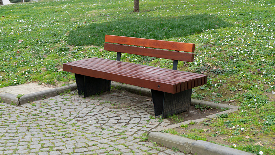 A brown wooden bench, next to flower beds with flowers in an urn in the park of the city of Kronstadt