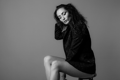 Beautiful female model posing with black jacket against gray background.