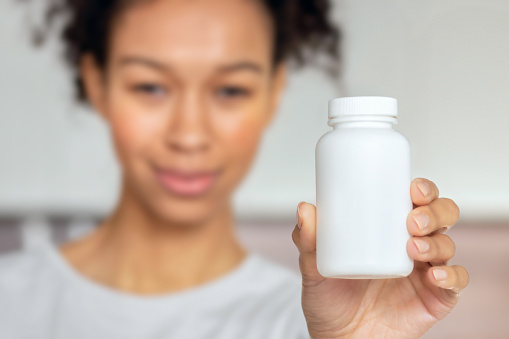 African American woman holding bottle of dietary supplements or vitamins in her hands close up, copy space. Healthy lifestyle concept