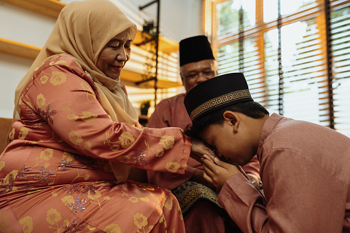 Muslim family celebrating Eid al-Fitr in hari raya attires, handshaking and asking forgiveness from each other