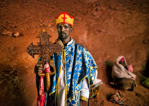 ETHIOPIA,LALIBELA,MARCH 2018--unidentified priest put the cross to pilgrim woman in biet Mariam.The 11 medieval monolithic cave churches of this 13th-century 'New Jerusalem' are situated in a mountainous region in the heart of Ethiopia near a traditional village with circular-shaped dwellings. Lalibela is a high place of Ethiopian Christianity, still today a place of pilmigrage and devotion.