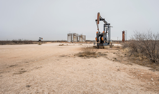 Oil well pumpjacks with storage tanks on the desert near Eunice, New Mexico