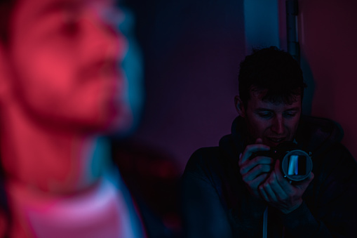 Two people in neon color indoors, person shooting with purple light on professional camera equipment. Camera man as operator, cinematic effect, lifestyle concept photography with selective focus.