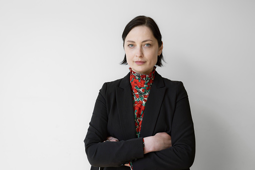 Portrait of a confident mature businesswoman standing against white wall. Female business professional with arms crossed looking at camera at office.