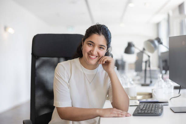Portrait of a confident young woman sitting at desk stock photo