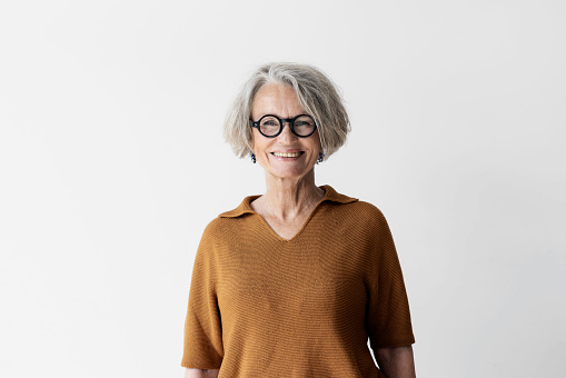 Portrait of confident senior woman with short hair wearing eyeglasses. Smiling mature female  standing against white wall.