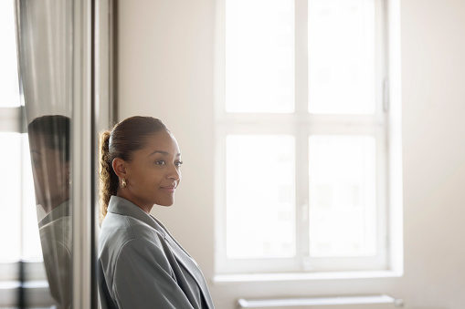 Portrait of a happy young african businesswoman standing in office. Female entrepreneur standing by window looking away and thinking at work.