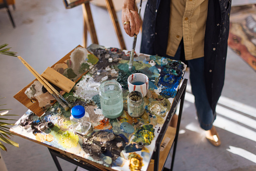 An artist and painter woman have a creative mess of paints and brushes on their desks