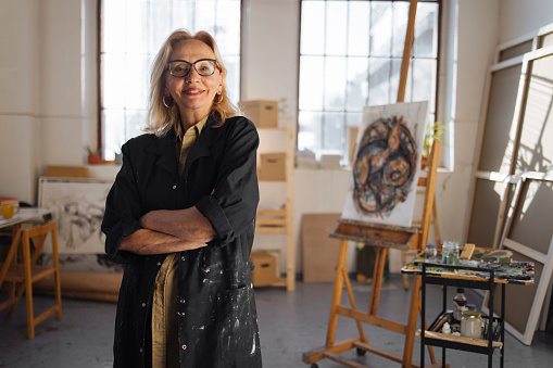 A confident female artist stands in her studio and poses for a portrait photo