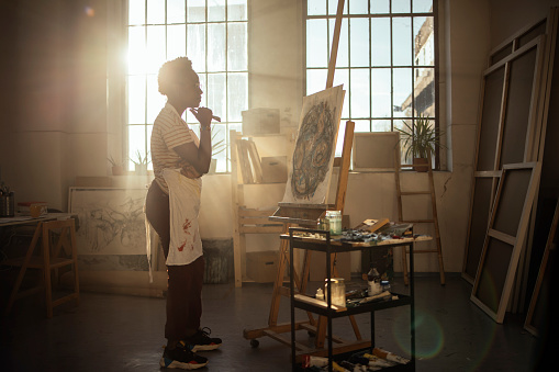 A ray of sunlight enters the art studio as a female artist paints