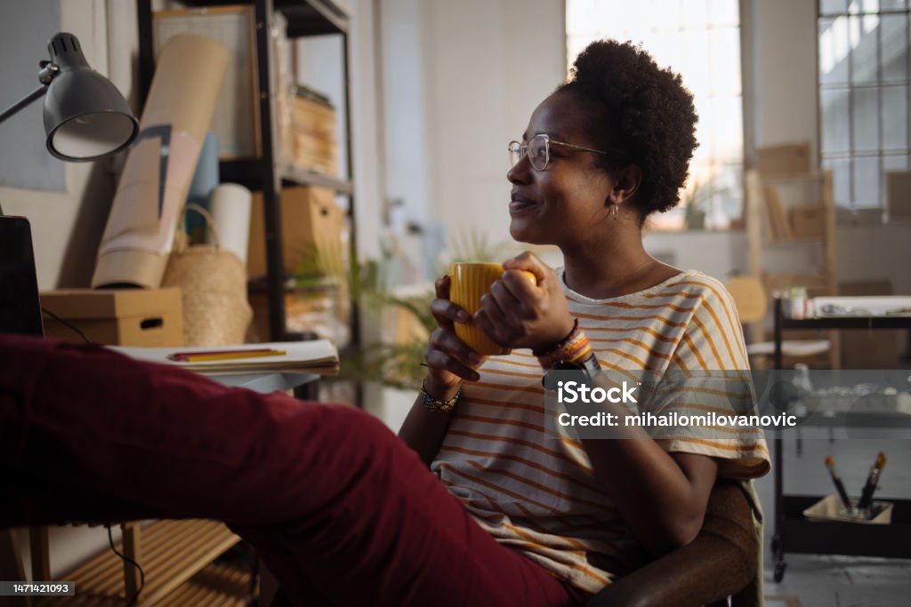 Earned break from work A young woman is enjoying her break by putting her feet up and enjoying her coffee while looking out the window 20-29 Years Stock Photo
