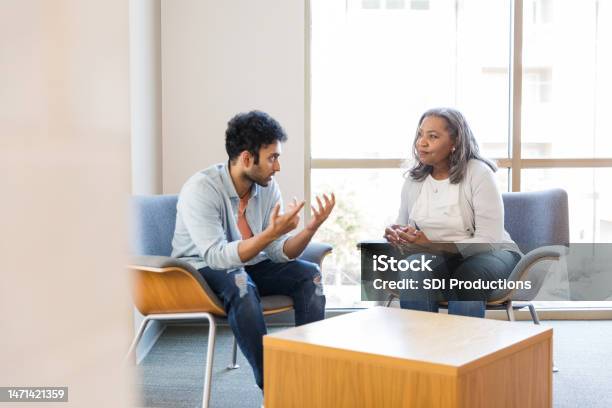 Young Man Gestures While Sharing With Female Counselor Stock Photo - Download Image Now