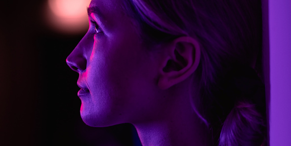 Female portrait in neon color indoors, person with purple, blue, red and pink light. Woman photo, lifestyle concept photography with multi coloured lights and colors.