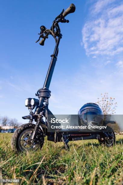 Photo Of One Black Electric Puch Scooter Outdoors Kickscooter On The Green Grass Near The Building Protective Helmet On The Deck Ecological Transport Concept Photography Lifestyle Photo Stock Photo - Download Image Now