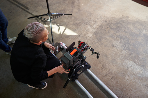 videographer sits on the floor next to a professional movie camera, sets the correct video angle. High quality photo