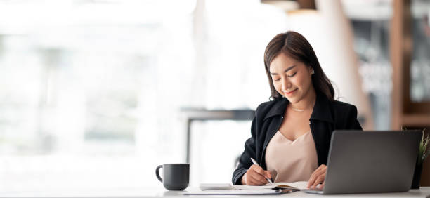 Attractive businesswoman using laptop writing business plan at desk in office, analyzing, accounting, statistics and research.