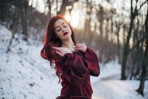 Beautiful young woman feeling cold in a snowy forest. Warming up her hands.