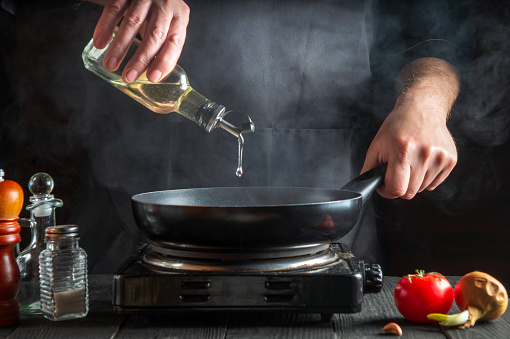 Chef or cook adds olive oil to the pan while cooking. Working environment on restaurant kitchen