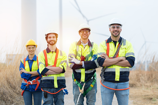 Portrait of male and female engineers wearing uniform and helmet preparing for working at wind turbines farm