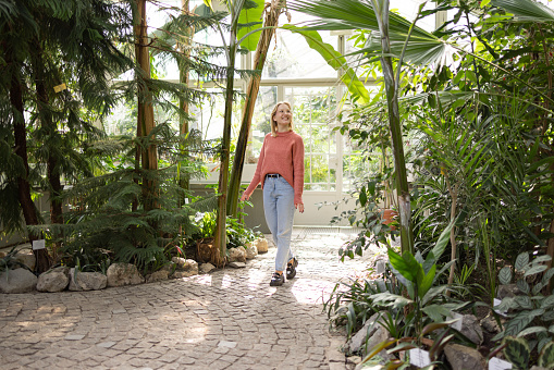 Young Caucasian woman walking trough a lush botanical garden, enjoying herself and smiling