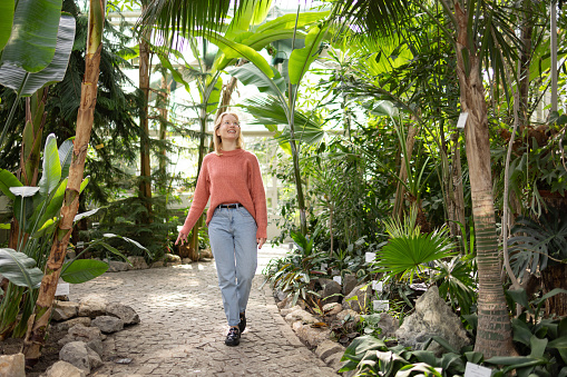 Woman enjoying the view surrounded with giant bananas leaves inside of Botanical Garden, while wearing urban jeans