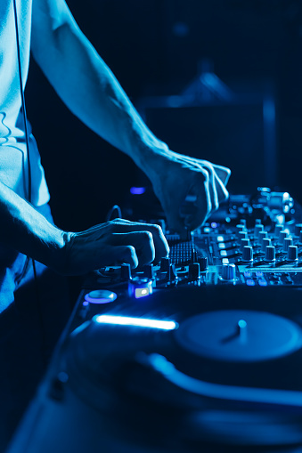 Night club DJ playing music with professional audio equipment on stage