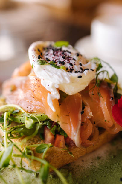 Salmon on a pillow of tomato on toast, and a poached egg on top, garnished with black sesame, spirulina and microgreens