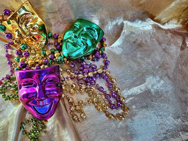 Traditional vibrant colors green gold purple, symbolic, Mardi Gras masks beads against shiny lamé background with space for copy.