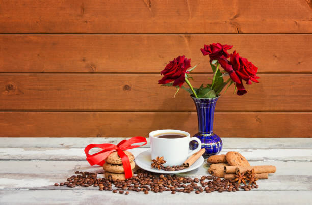 taza de café, galletas, especias, granos de café y rosas rojas sobre una mesa de madera envejecida. - coffee bean coffee flower ribbon fotografías e imágenes de stock