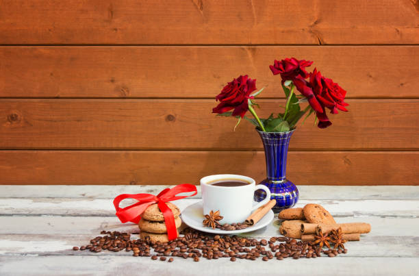 чашка кофе, печенья, специй, кофейных зерен и красных роз на выдержанном деревянном столе. - coffee bean coffee flower ribbon стоковые фото и изображения
