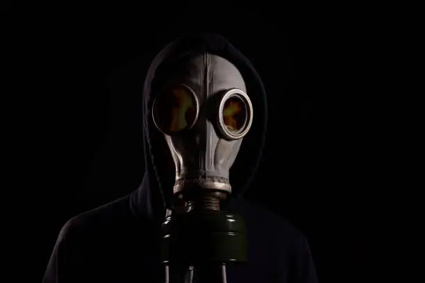 Photo of A man in a hood in a gas mask with a reflection of fire in the glasses. The concept of a fire.