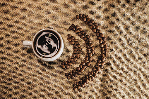 Fresh roasted coffee beans in form of W-iFi and hot cup of coffeeon a burlap bag on the table .