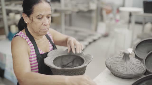 Woman shaping an ornate bowl using a knife in a ceramics factory