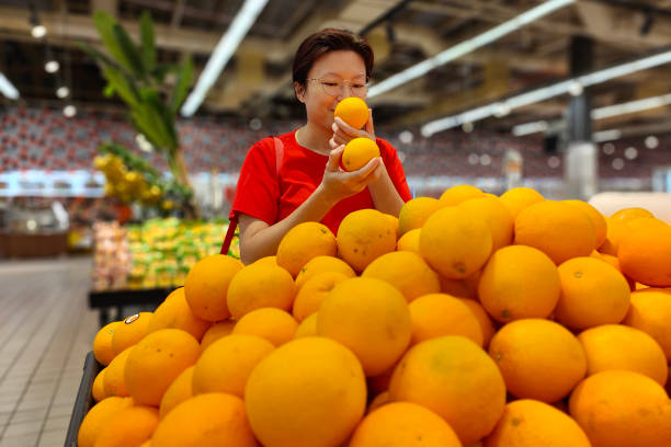 An Asian woman is selecting fresh oranges in supermarket