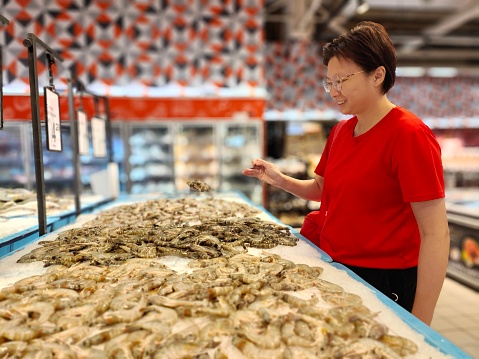 An Asian woman is selecting fresh prawn in supermarket