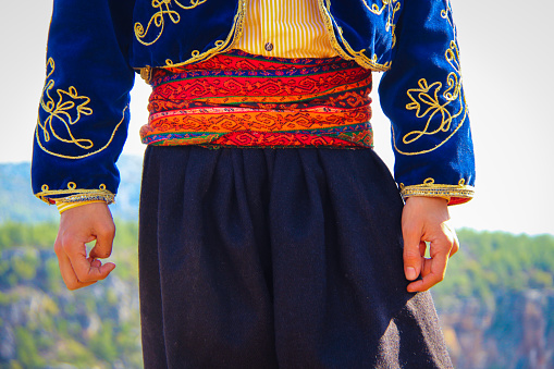 a man plays folk dance in local dress in nature.\n\nman playing the traditional dance zeybek.