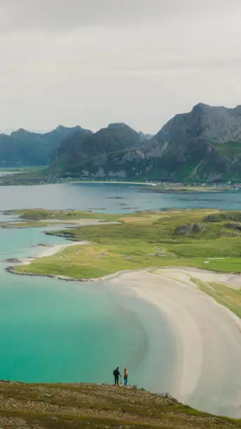 Photo of Aerial view of woman and man contemplating scenic view of the ocean and mountains from top of Lofoten Islands