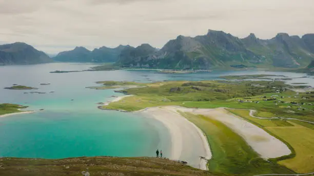 Photo of Aerial view of woman and man contemplating scenic view of the ocean and mountains from top of Lofoten Islands