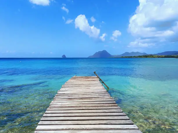 Photo of Pier at beach in Landscape of the French West Indies. The wooden bridge stretches into the sea. Beautiful tropical with Mountain clouds and sky.