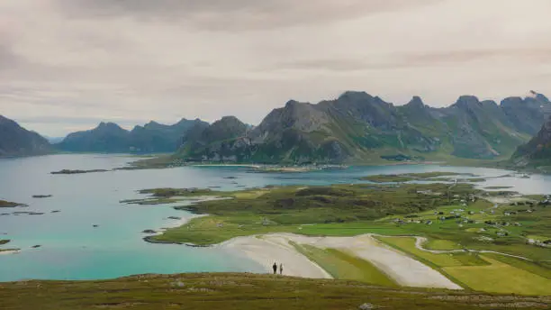 Photo of Aerial view of woman and man contemplating scenic view of the ocean and mountains from top of Lofoten Islands