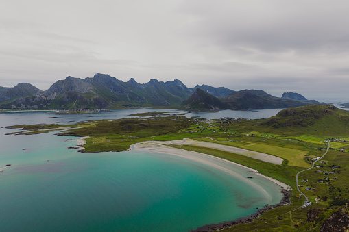 Scenic landscape with the turquoise colored ocean, white sand beach and the tiny village by the beautiful mountains in Northern Norway