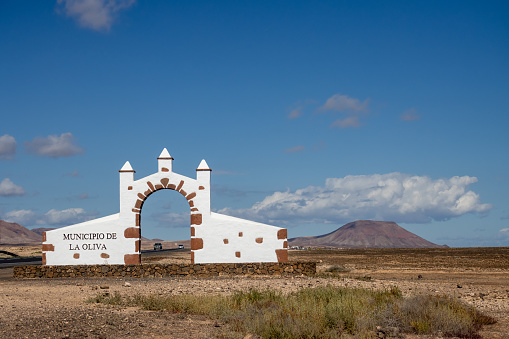 Entrance to every municipality of the island has a gate.This one is for Municipality of la Oliva (Municipio de la Oliva). Built beside a road. Mountain in the background. Fuerteventura, Canary Islands