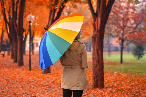 A young woman walks with a colorful umbrella in hand walking in the autumn.